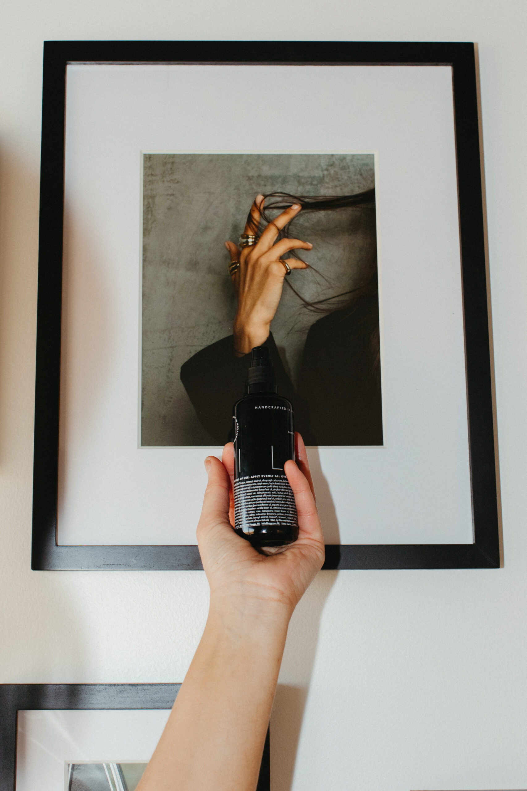Bottle of Reverie Hair Care Product in front of frame photo of woman twirling hair.